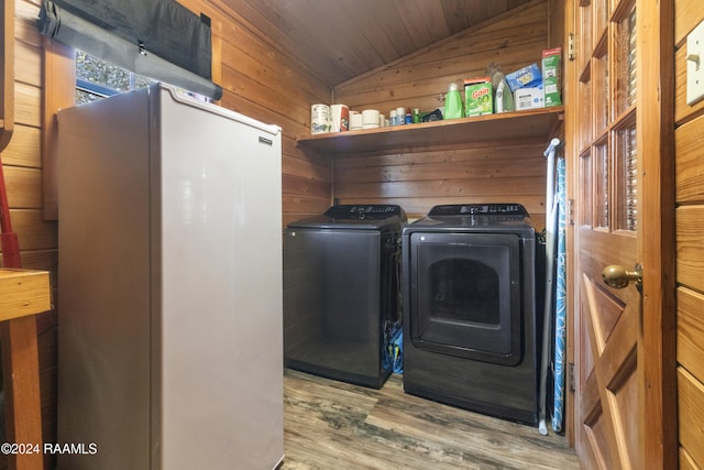 laundry area with hardwood / wood-style flooring, wood walls, and washing machine and clothes dryer