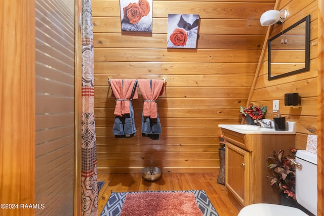 bathroom featuring vaulted ceiling, toilet, wooden walls, vanity, and hardwood / wood-style flooring