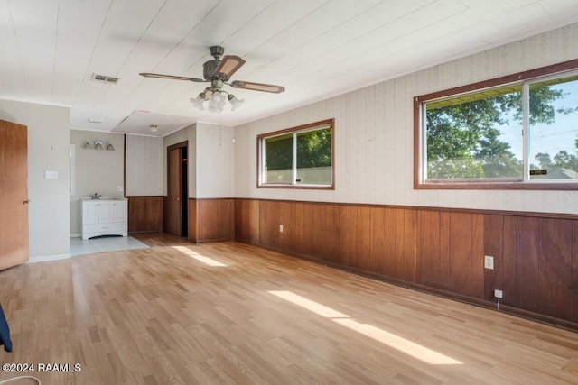 unfurnished room with ceiling fan, wooden walls, light hardwood / wood-style floors, and a healthy amount of sunlight