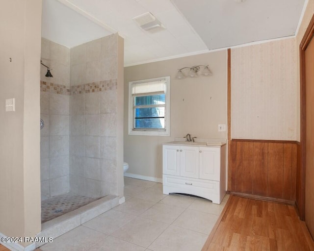 bathroom featuring a tile shower, vanity, wooden walls, and toilet