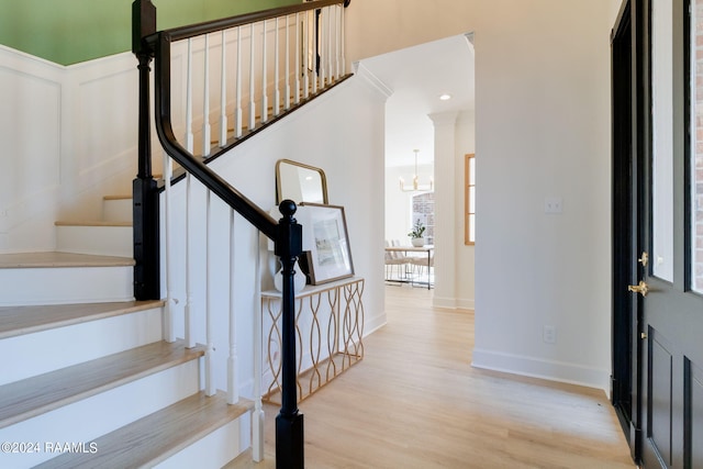 foyer featuring light hardwood / wood-style floors, decorative columns, and an inviting chandelier