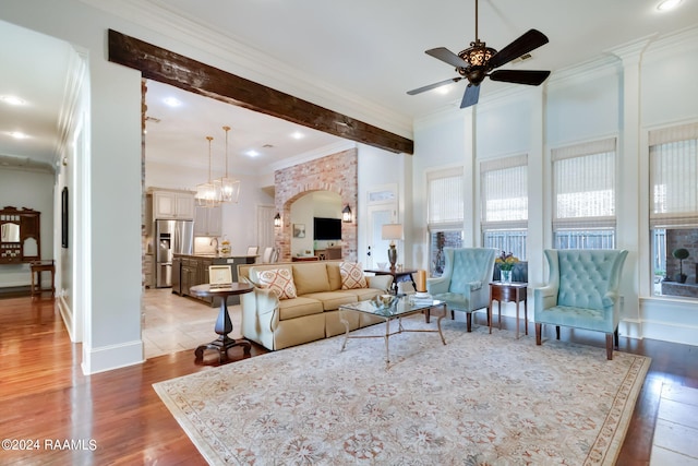 living room with wood-type flooring, ceiling fan with notable chandelier, crown molding, and beam ceiling