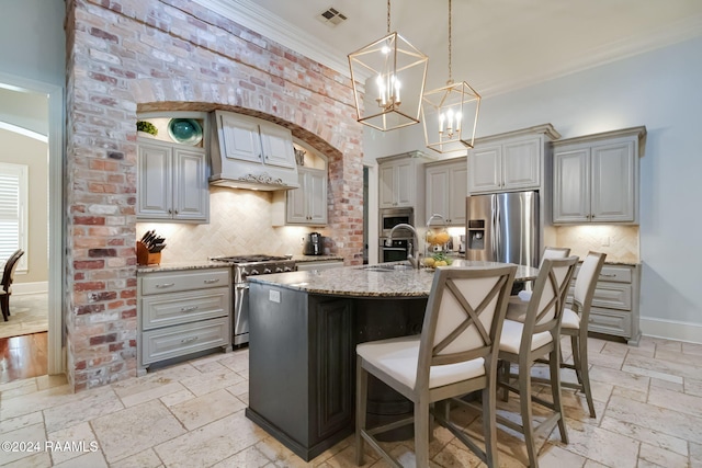 kitchen with a center island with sink, appliances with stainless steel finishes, a kitchen bar, and gray cabinetry