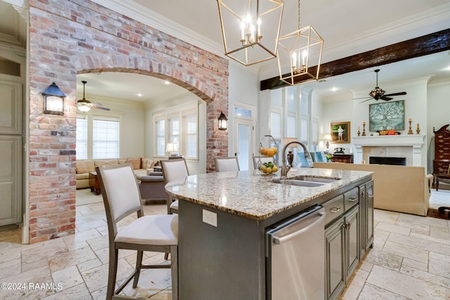 kitchen featuring a kitchen island with sink, beam ceiling, sink, light stone countertops, and hanging light fixtures