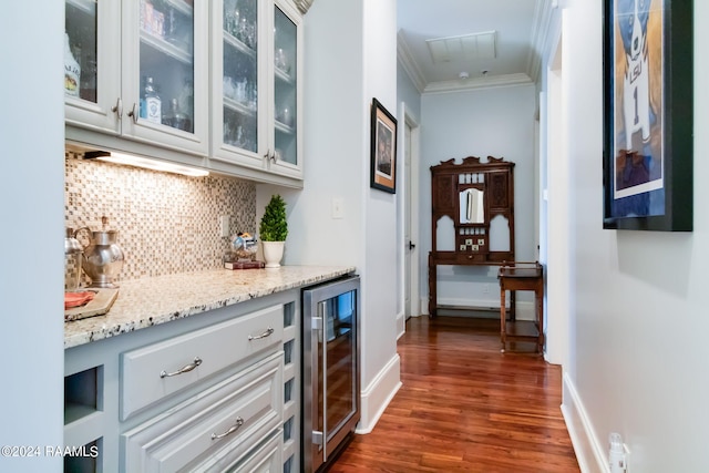 bar with light stone counters, white cabinets, wine cooler, ornamental molding, and dark hardwood / wood-style flooring