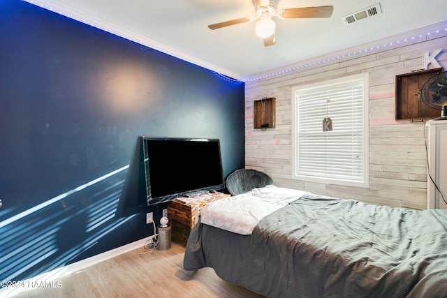 bedroom with ceiling fan, light wood-type flooring, crown molding, and wood walls