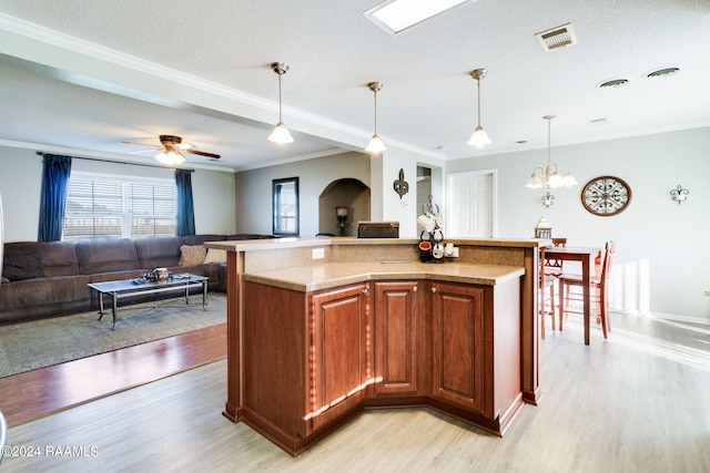 kitchen featuring ceiling fan with notable chandelier, light hardwood / wood-style flooring, a center island with sink, hanging light fixtures, and ornamental molding