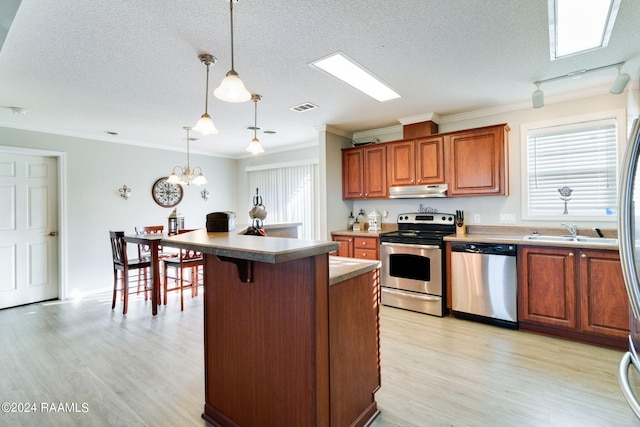 kitchen with appliances with stainless steel finishes, pendant lighting, light hardwood / wood-style floors, and extractor fan