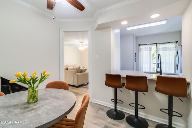 dining room with wood finished floors, a ceiling fan, ornamental molding, and baseboards