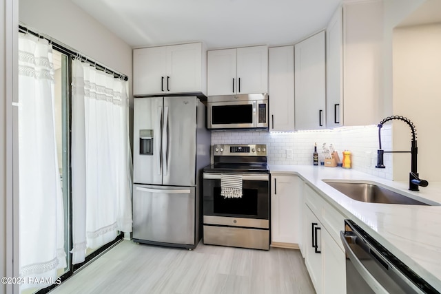kitchen featuring tasteful backsplash, light stone countertops, stainless steel appliances, a sink, and white cabinetry
