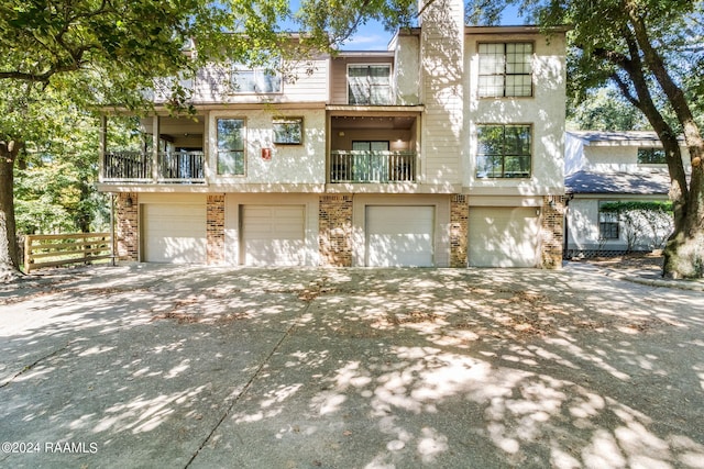 view of front of property with a garage, a balcony, brick siding, concrete driveway, and stucco siding