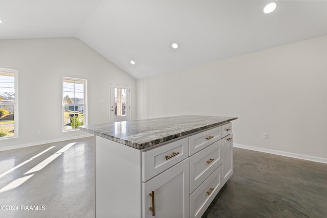 kitchen with stone countertops, a kitchen island, white cabinetry, and vaulted ceiling