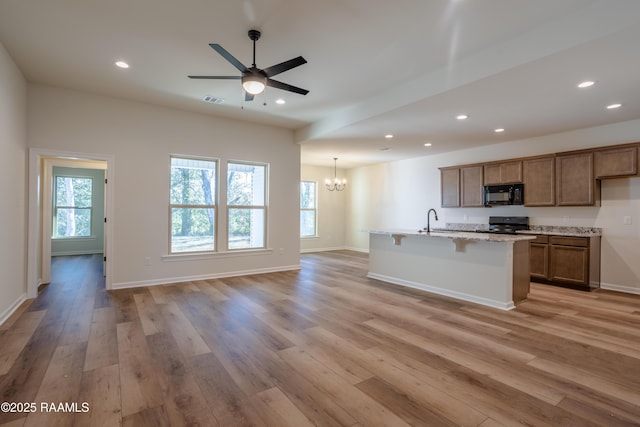 kitchen with ceiling fan with notable chandelier, an island with sink, light wood-type flooring, and black appliances