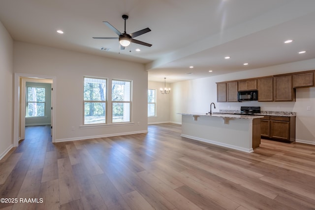 kitchen featuring black appliances, a healthy amount of sunlight, an island with sink, and light wood-type flooring