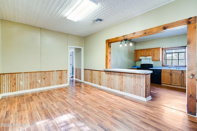 kitchen featuring light hardwood / wood-style floors, kitchen peninsula, black appliances, and wooden walls