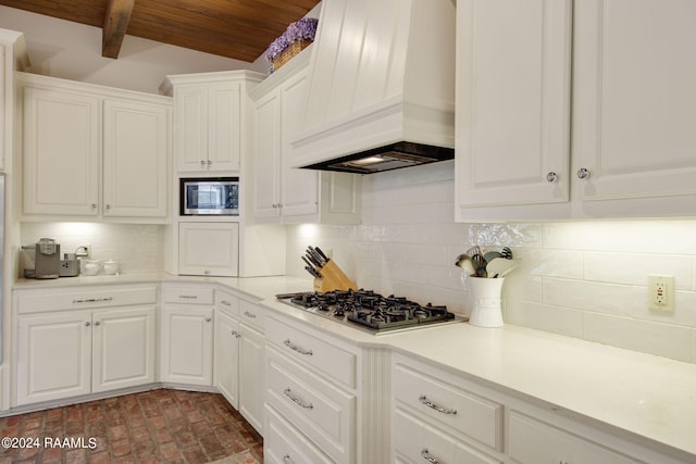 kitchen with appliances with stainless steel finishes, white cabinets, beam ceiling, and premium range hood