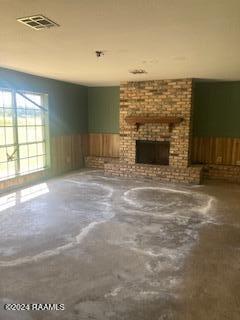 unfurnished living room with a wainscoted wall, a fireplace, concrete floors, and visible vents