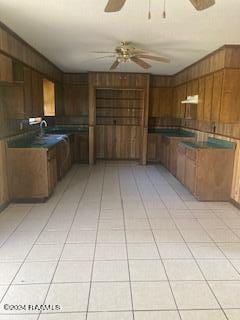 kitchen with dark countertops, wooden walls, under cabinet range hood, a ceiling fan, and light tile patterned floors