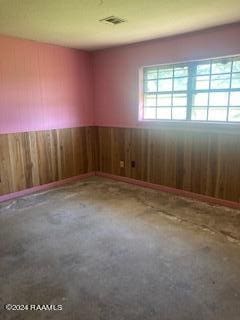 empty room featuring wooden walls, a wainscoted wall, and visible vents
