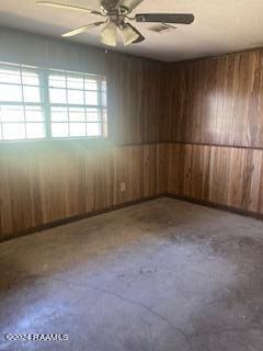 unfurnished room with ceiling fan, concrete flooring, and wood walls