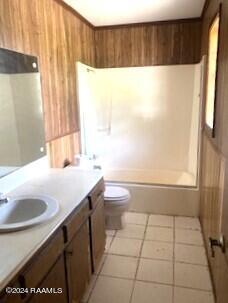 bathroom featuring vanity, tile patterned flooring, shower / bathtub combination, toilet, and wooden walls