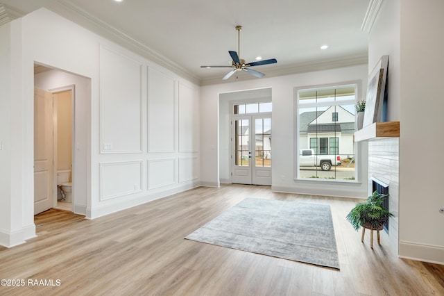 living area featuring light wood-style floors, a fireplace, a decorative wall, and crown molding