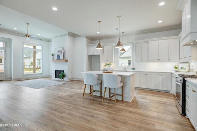 kitchen with decorative light fixtures, open floor plan, white cabinetry, a kitchen island, and gas range