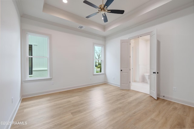 empty room featuring light wood-style floors, a raised ceiling, and ornamental molding