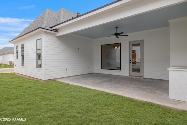 view of exterior entry with a yard, a shingled roof, a patio area, and a ceiling fan