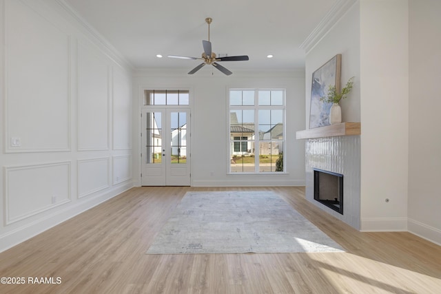 interior space with a fireplace, light wood finished floors, a decorative wall, ornamental molding, and baseboards