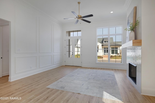 doorway featuring light wood finished floors, a ceiling fan, a glass covered fireplace, ornamental molding, and a decorative wall