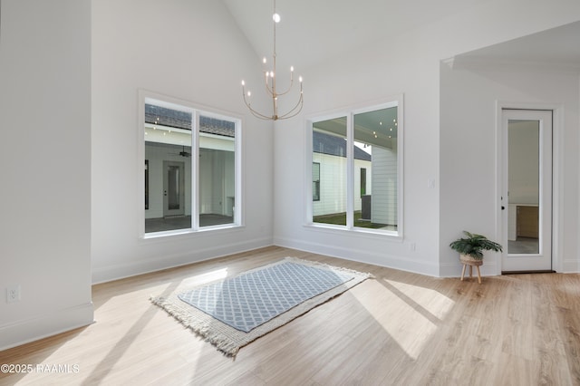 interior space featuring light wood-style floors, a notable chandelier, high vaulted ceiling, and baseboards