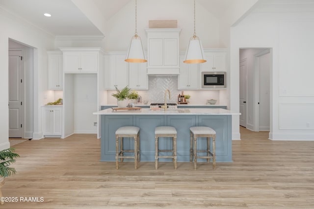 kitchen with light countertops, hanging light fixtures, a center island with sink, and built in microwave