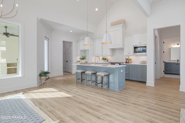 kitchen featuring light countertops, stainless steel microwave, gray cabinetry, a kitchen island with sink, and white cabinetry