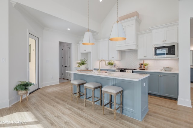 kitchen featuring black microwave, a kitchen island with sink, white cabinetry, a kitchen breakfast bar, and pendant lighting