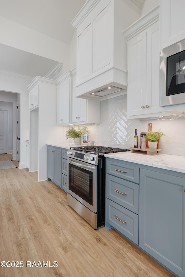 kitchen featuring premium range hood, stainless steel range with gas cooktop, built in microwave, and white cabinets