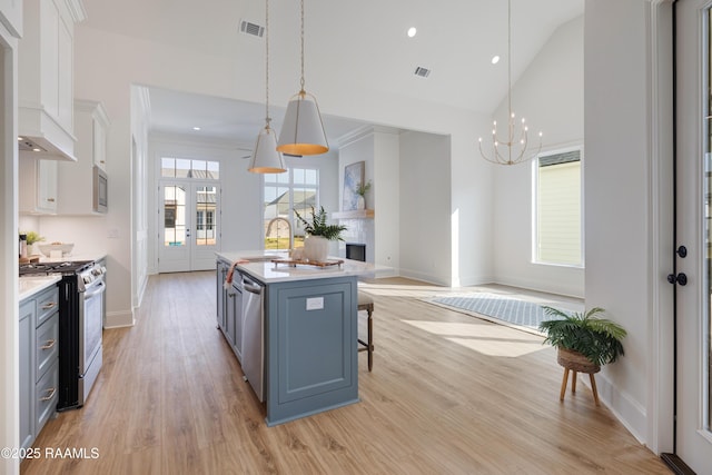 kitchen featuring stainless steel appliances, white cabinetry, light countertops, an island with sink, and decorative light fixtures