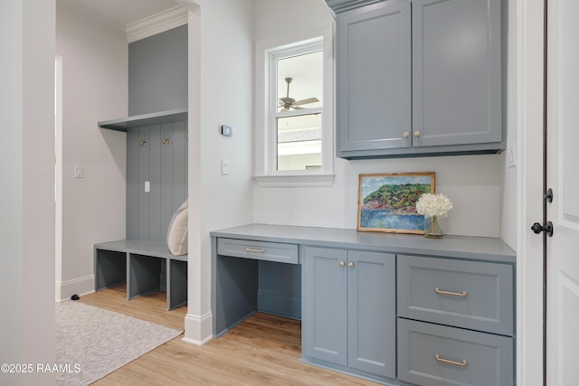 mudroom with light wood-type flooring, crown molding, built in desk, and baseboards