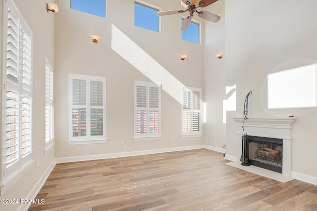 201 Settlers Trace Blvd Unit 2401, Lafayette, LA 70508 - unfurnished living room featuring ceiling fan, light wood-type flooring, a high ceiling, a fireplace with flush hearth, and baseboards