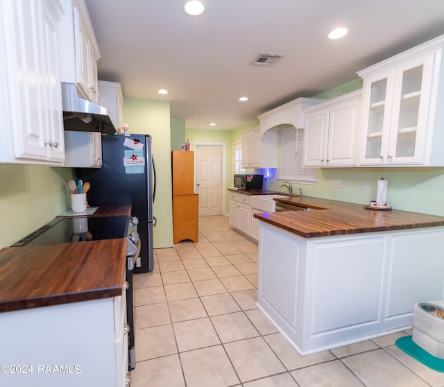 kitchen featuring butcher block countertops, light tile patterned floors, and white cabinets