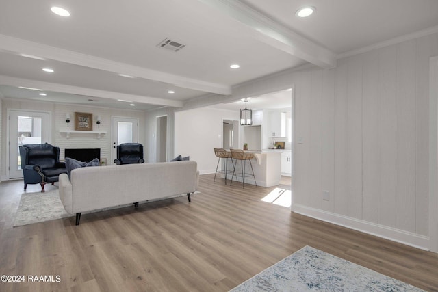 living room with beamed ceiling, ornamental molding, wood-type flooring, and a large fireplace