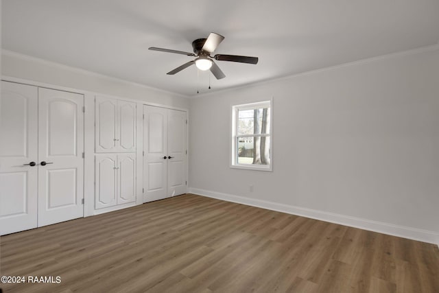 unfurnished bedroom featuring ceiling fan, ornamental molding, wood-type flooring, and two closets