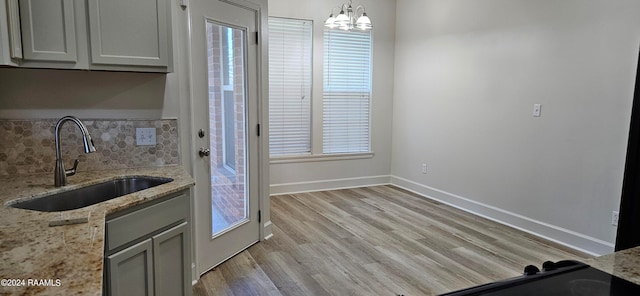 kitchen featuring decorative backsplash, hanging light fixtures, light stone countertops, light wood-type flooring, and sink