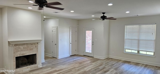 unfurnished living room featuring a tiled fireplace, ceiling fan, and light hardwood / wood-style flooring