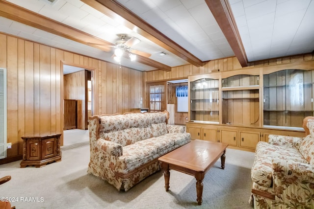 carpeted living room featuring beam ceiling, wood walls, and ceiling fan