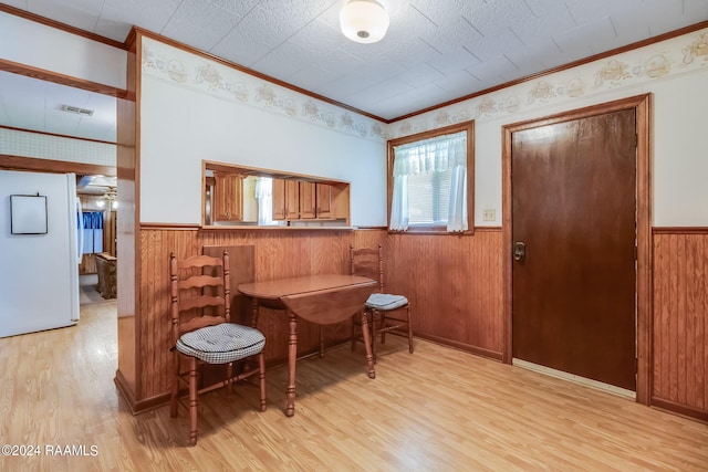 dining space featuring light hardwood / wood-style floors, ornamental molding, and wooden walls