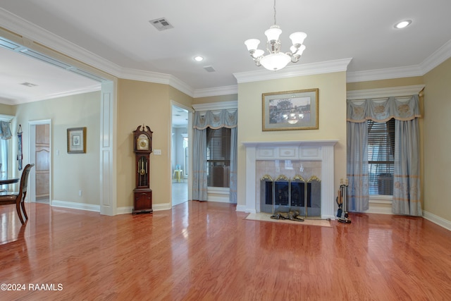 unfurnished living room with an inviting chandelier, ornamental molding, a tile fireplace, and light hardwood / wood-style floors