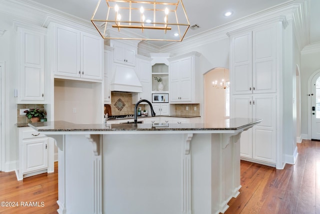 kitchen featuring a kitchen island with sink, light wood-type flooring, white cabinets, and dark stone countertops