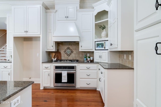 kitchen featuring custom range hood, dark stone counters, white cabinets, appliances with stainless steel finishes, and tasteful backsplash