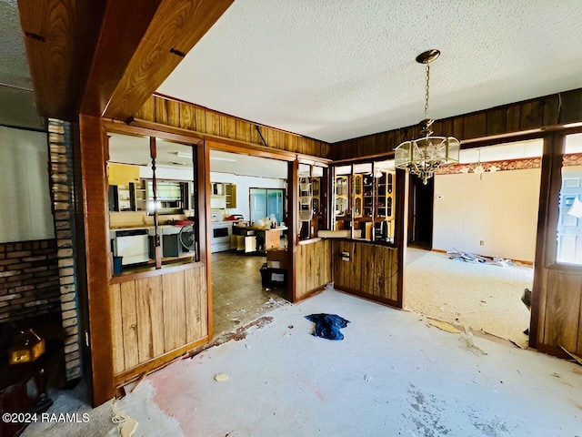 dining room featuring wooden walls, concrete flooring, a textured ceiling, and an inviting chandelier